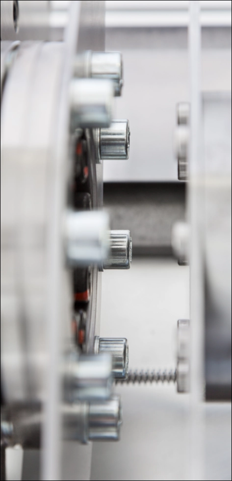 Detailaufnahme einer hochpräzisen Schwingprüfanlage (Vibrationsprüfsystem) mit Fokus auf den zentralen Prüfschlitten und die metallische Führungskonstruktion in blau-schwarzer technischer Beleuchtung.