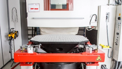 Industrielles Vibrationsprüfsystem mit einem oktogonalen Schwingtisch auf einem roten Metallrahmen vor einer weißen Klimakammer.