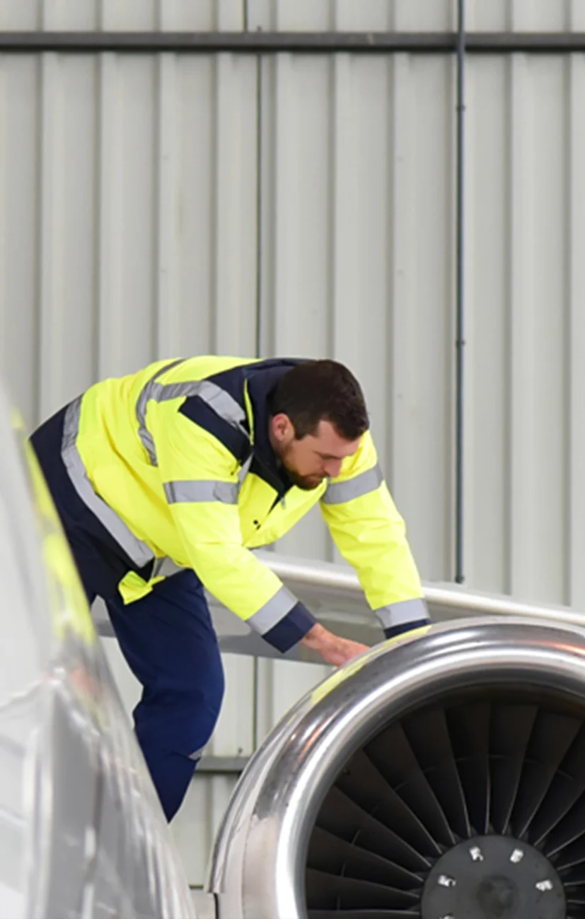 Techniker in Warnschutzkleidung bei der Inspektion eines Flugzeugtriebwerks in einer Industriehalle