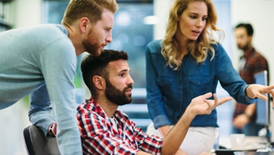 Drei junge Büroangestellte blicken gemeinsam auf einen Monitor und diskutieren konzentriert in einer modernen Arbeitsumgebung.