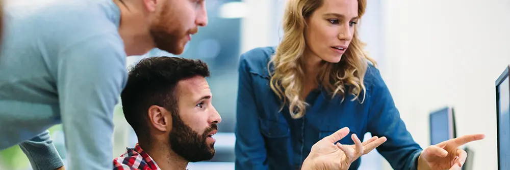 Drei Mitarbeitende im Büro besprechen gemeinsam Inhalte auf einem Bildschirm
