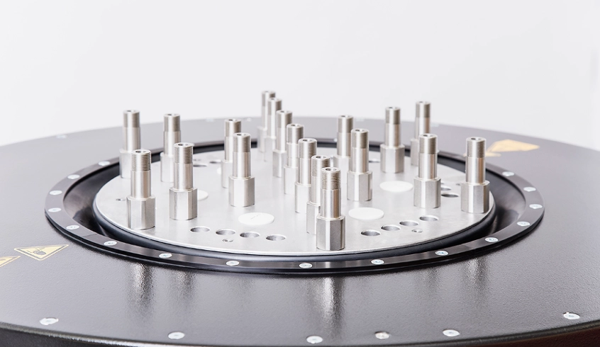 Nahaufnahme einer runden Prüfaufnahme mit mehreren metallischen Gewindebolzen auf einem technischen Prüfsystem.